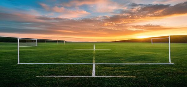 Football on green pitch with goalposts at sunrise