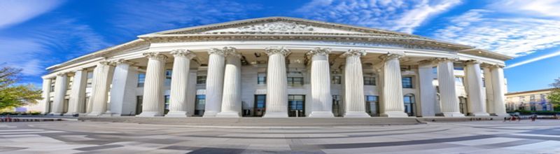 Panoramic view of the Marriner S. Eccles Federal Reserve Board building in Washington at midday, white neoclassical limestone facade with tall columns and central pediment, broad stone plaza in foreground, no people no faces no hands