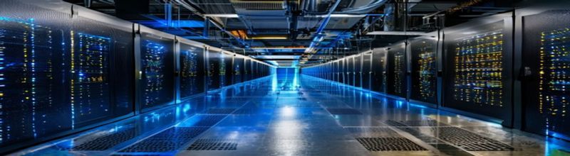Panoramic view of a server rack room with rows of dark cabinets and tiny green and blue indicator LEDs glowing in the dim light, polished concrete floor in the foreground, no people no faces no hands